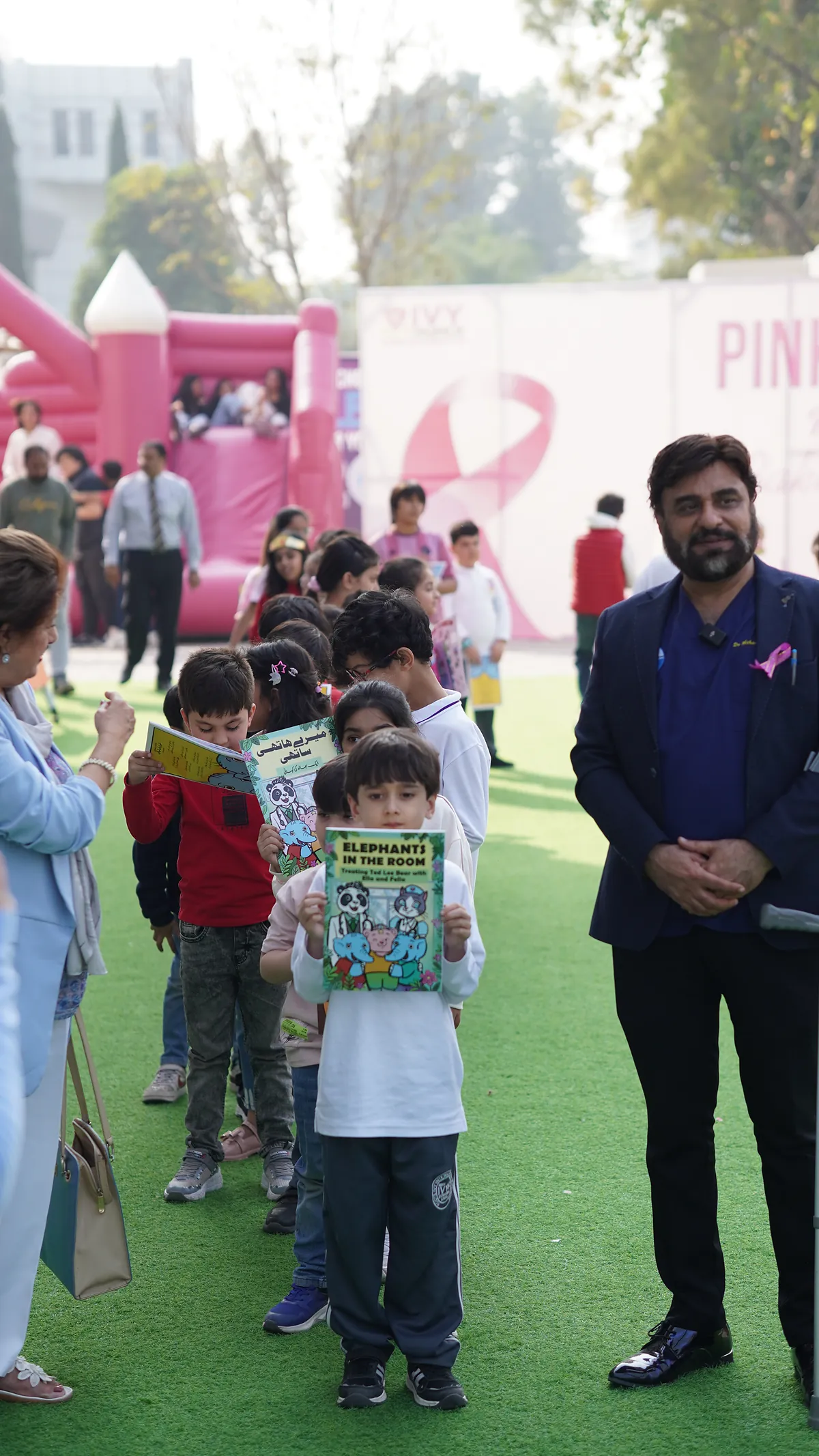 Young children walk across the school field carrying Killing Cancer Kindly comics at a Pinktober event.