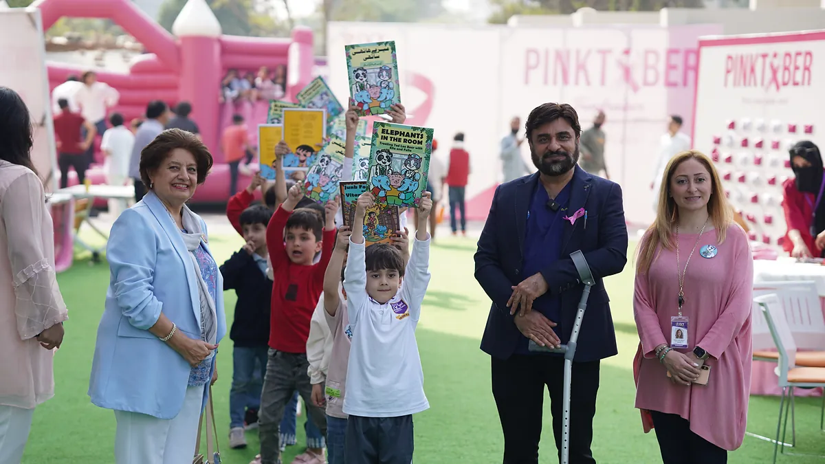 Children hold Killing Cancer Kindly comics above their heads at a school Pinktober awareness day.
