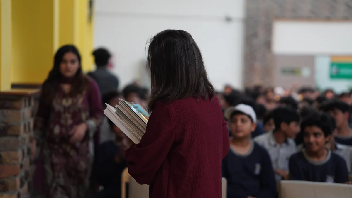 Volunteers walk the rows of a school hall handing out Killing Cancer Kindly comics to pupils.
