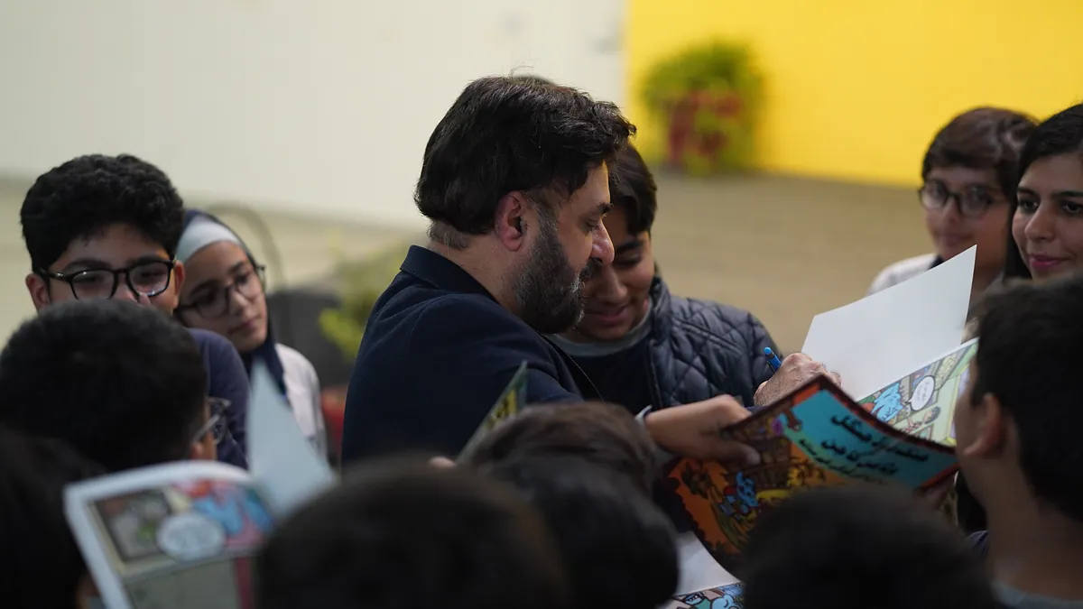 Dr Mohammad Muneeb Khan leans in among a group of pupils reading their comics together.