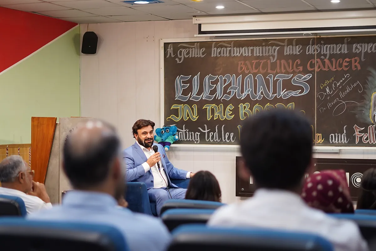 Dr Mohammad Muneeb Khan on stage at the Elephants in the Room launch, hand-lettered chalkboard behind him.