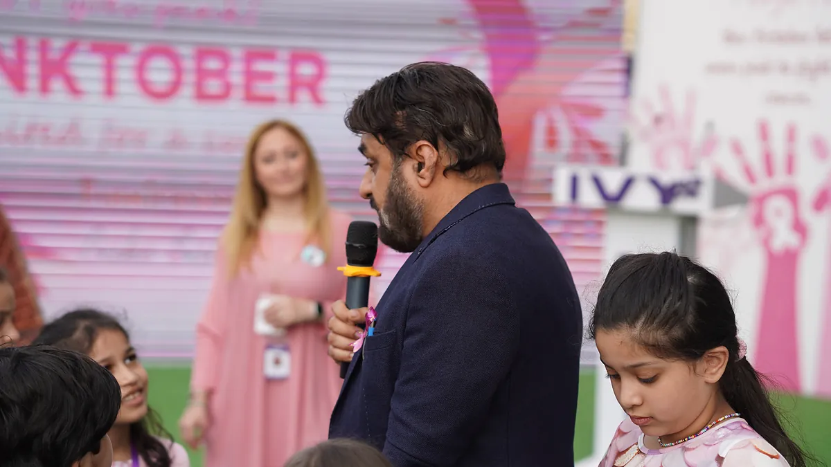 Dr Mohammad Muneeb Khan speaks into a microphone at a school Pinktober breast-cancer awareness event.