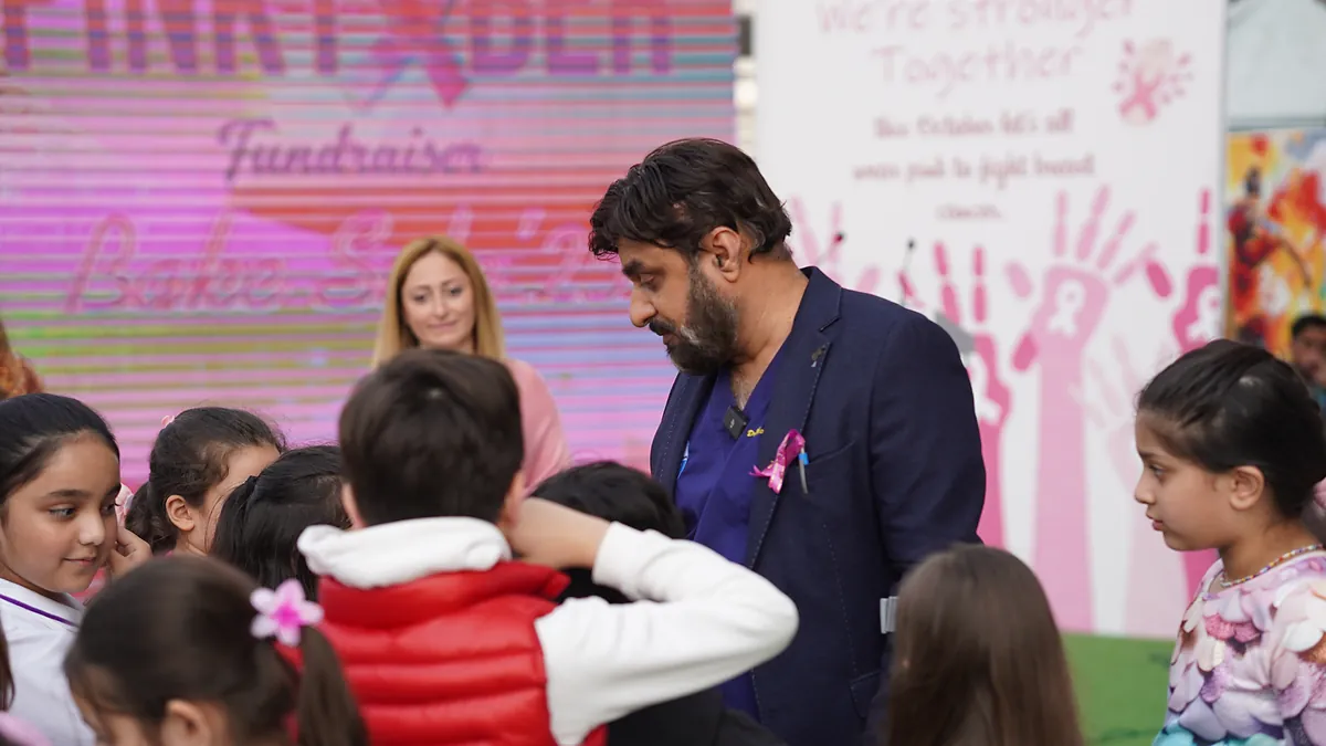 Dr Mohammad Muneeb Khan with schoolchildren in front of a Pinktober breast-cancer awareness backdrop.