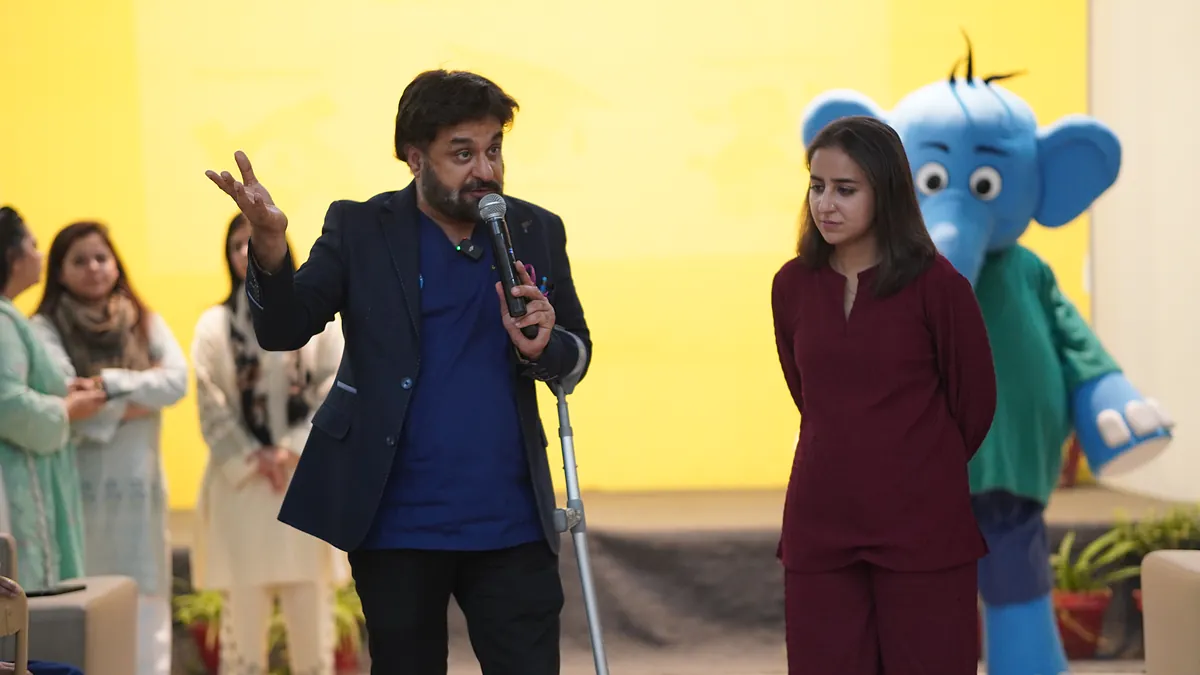A host introduces the Killing Cancer Kindly elephant mascot on stage as pupils watch from the hall.
