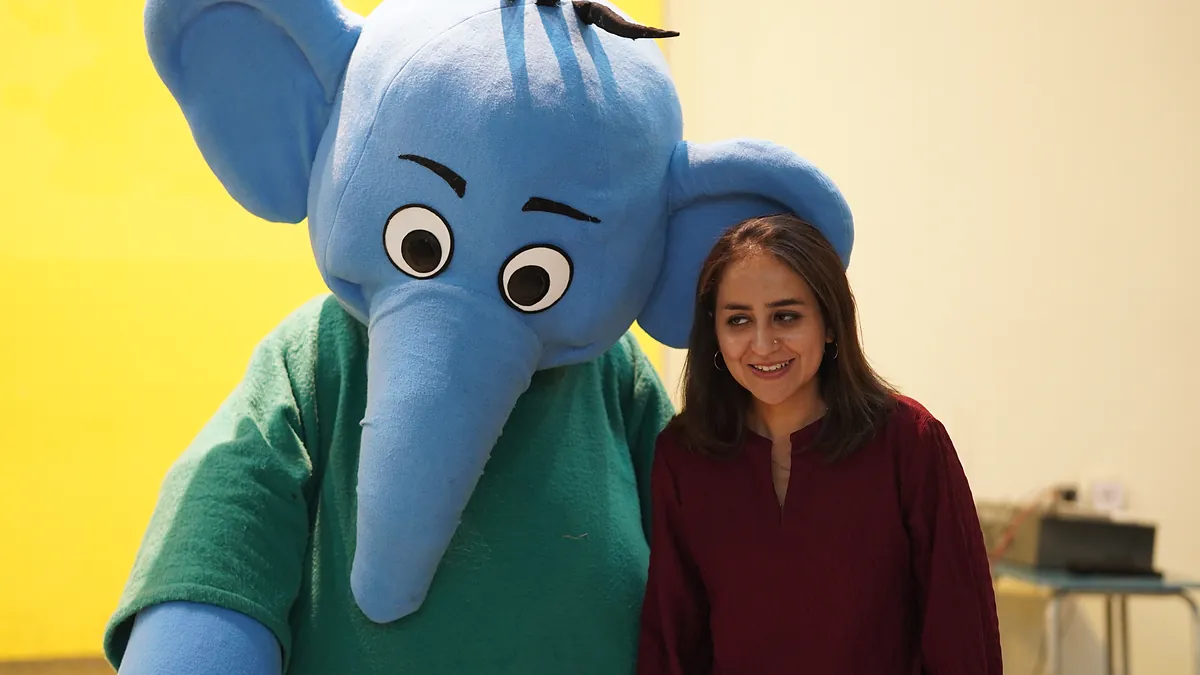 The Killing Cancer Kindly blue elephant mascot on stage beside a host at a school assembly.