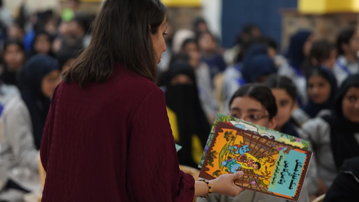A Killing Cancer Kindly volunteer hands a prevention comic to a pupil seated in the school hall.