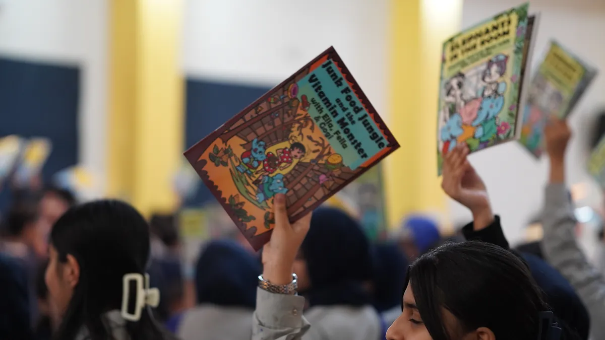 Two Killing Cancer Kindly comic titles held up side by side by pupils in a school assembly.